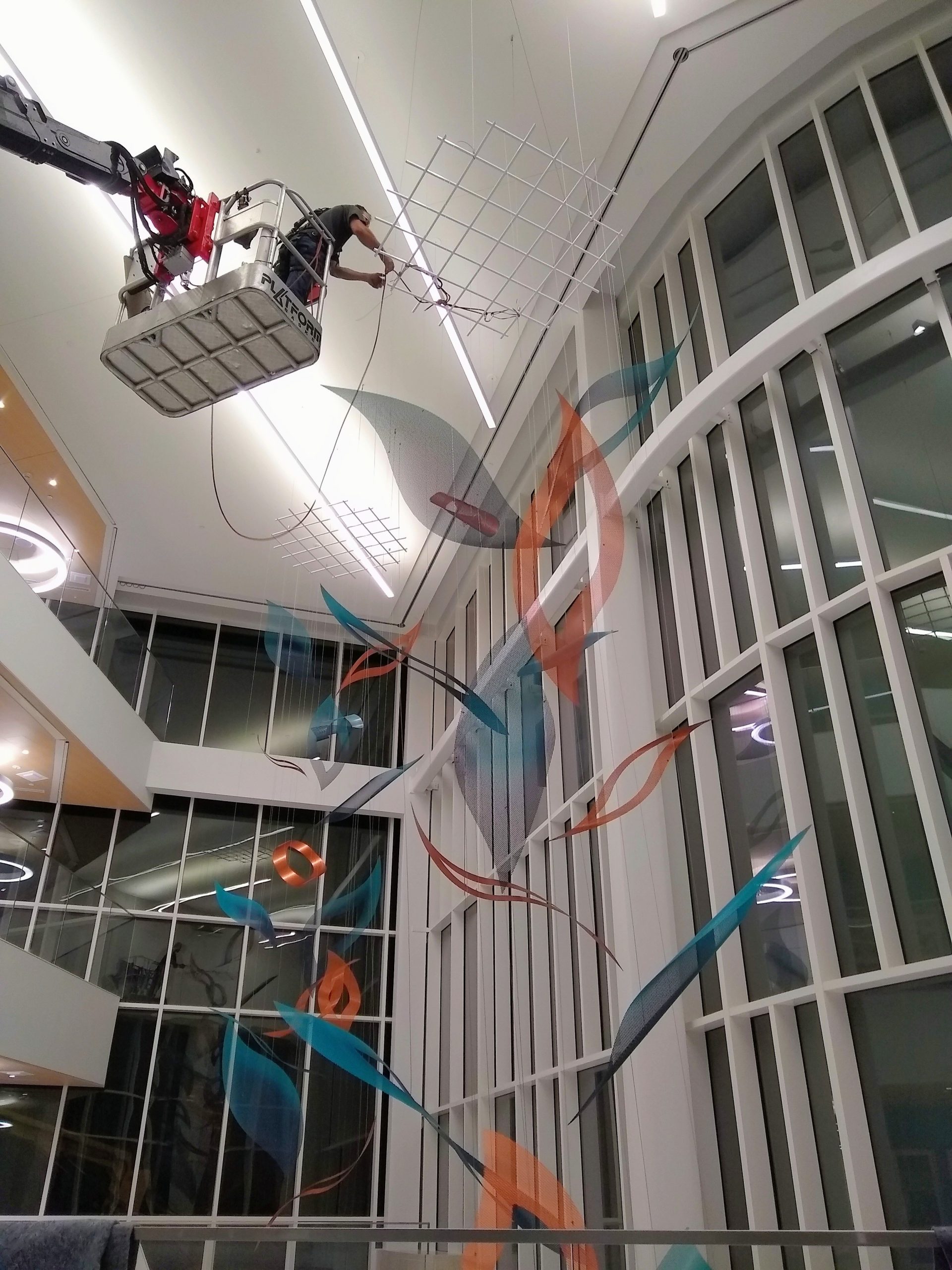An art rigger in an aerial lift installs cables to a grid suspending the atrium sculpture.